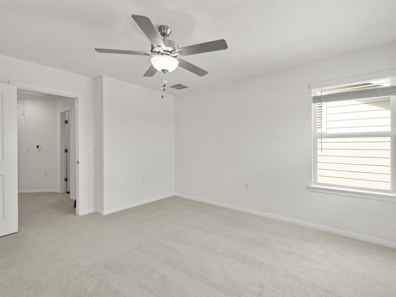 A well-lit bedroom with soft carpet and a modern ceiling fan, offering a tranquil retreat.