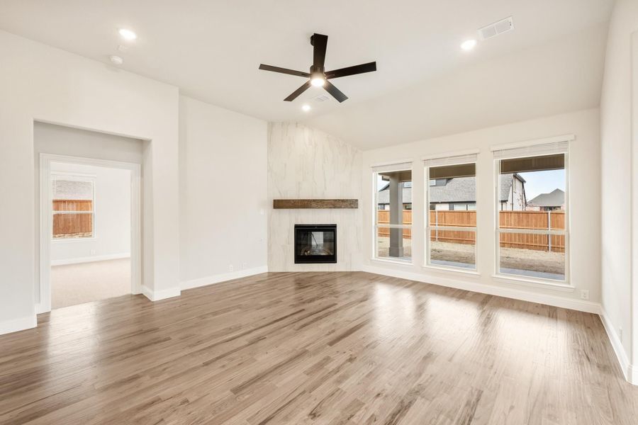 Empty living room with hardwood floors, marble fireplace, ceiling fan, and large windows