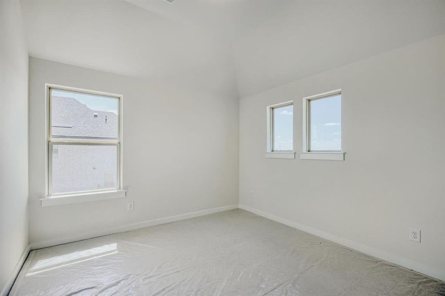 Neutral-toned interior room featuring a vaulted ceiling and multiple windows