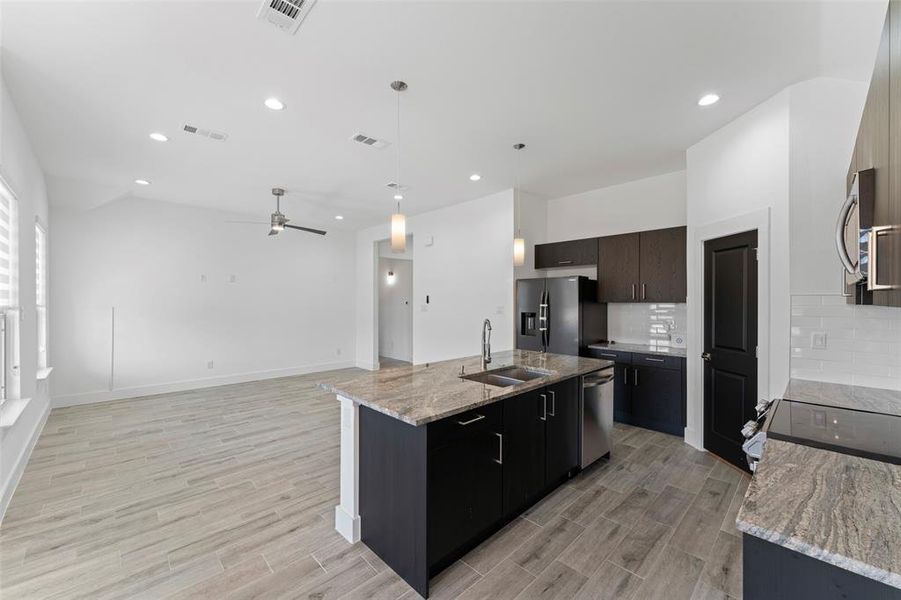 Kitchen featuring appliances with stainless steel finishes, ceiling fan, a kitchen island with sink, sink, and decorative light fixtures