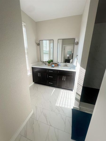 Ensuite bathroom with light marble finish flooring, double vanity, and a textured wall