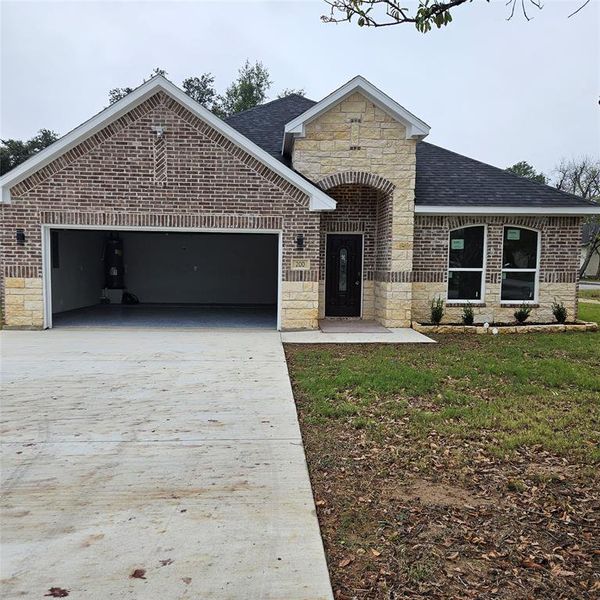featuring stone siding, concrete driveway, brick siding, and roof with shingles