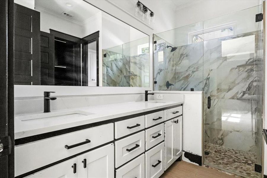 Bathroom featuring ornamental molding, a marble finish shower, and double vanity