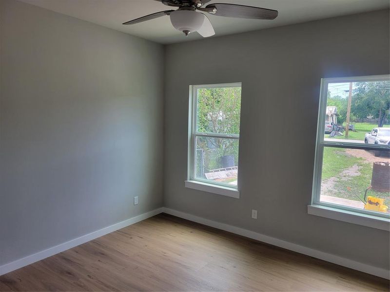 Interior room featuring wood-finish flooring, two window openings, and a ceiling fan with integrated lighting