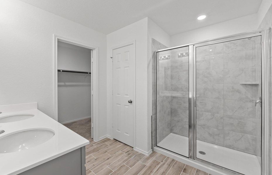 Bathroom with double vanity, a shower stall, a spacious closet, and wood finish floors Bathroom with double vanity, a shower stall, a spacious closet, and wood finish floors