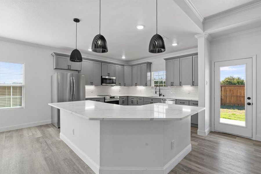 Kitchen featuring appliances with stainless steel finishes, light stone counters, decorative light fixtures, light hardwood / wood-style flooring, and a kitchen island