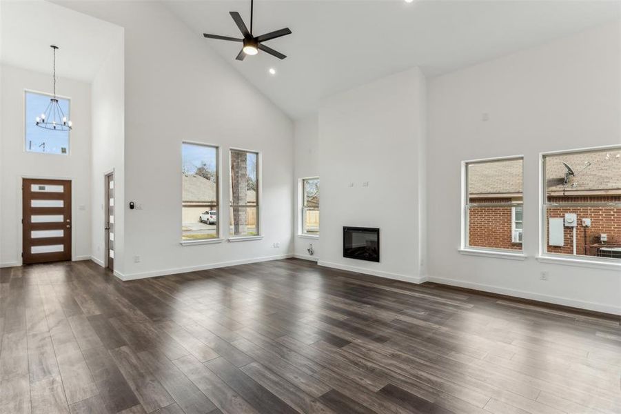 Unfurnished living room with a healthy amount of sunlight, dark wood-type flooring, ceiling fan with notable chandelier, and high vaulted ceiling