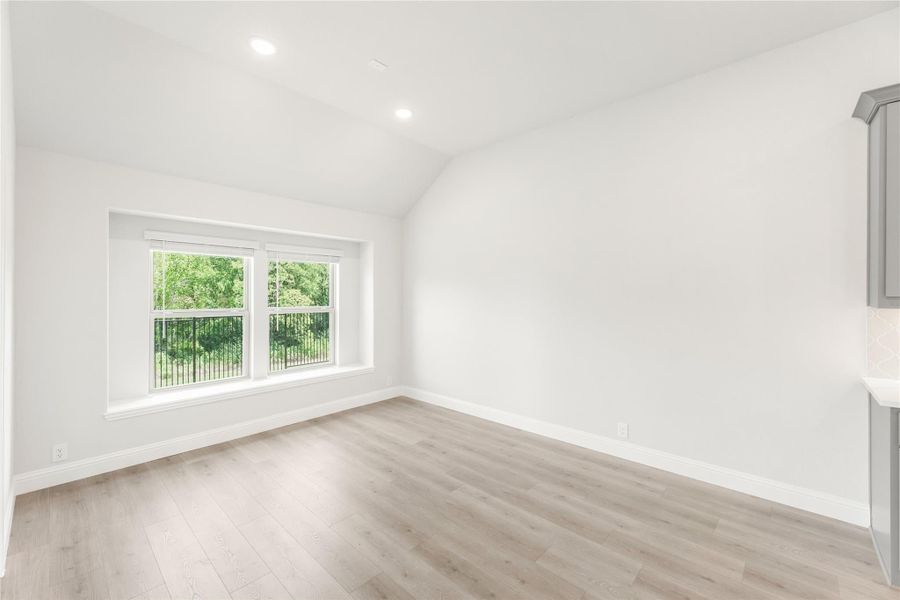 Empty room with vaulted ceiling, light wood floors, and double window with outdoor view Empty room with vaulted ceiling, light wood floors, and double window with outdoor view