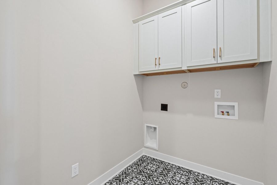 Laundry area featuring white shaker-style cabinetry with gold-toned hardware, light gray walls, and patterned floor tile Laundry area featuring white shaker-style cabinetry with gold-toned hardware, light gray walls, and patterned floor tile