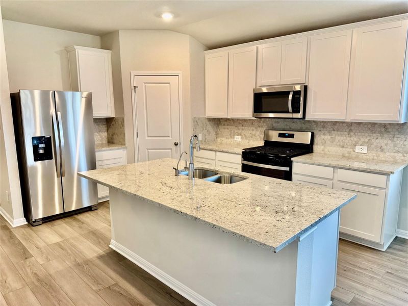 Kitchen featuring appliances with stainless steel finishes, light wood-style flooring, white cabinets, backsplash, and light stone countertops