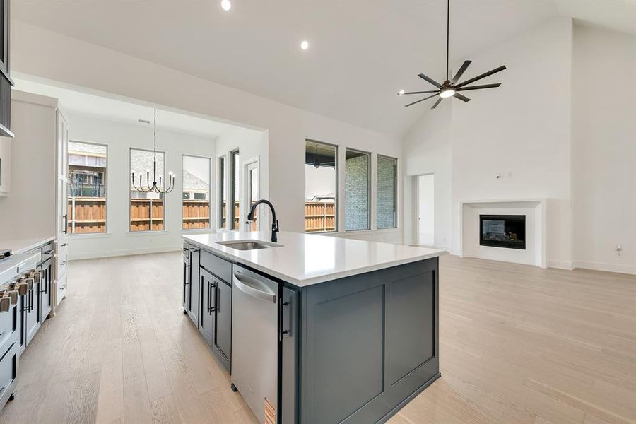 Kitchen featuring light wood finished floors, an island with sink, high vaulted ceiling, a chandelier, and appliances with stainless steel finishes Kitchen featuring light wood finished floors, an island with sink, high vaulted ceiling, a chandelier, and appliances with stainless steel finishes