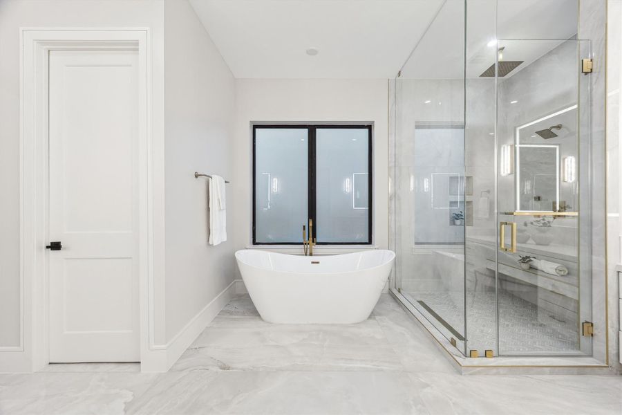 The luxurious primary bath features a free standing tub and a spacious walk-in shower with framless glass enclosure and a built-in bench.