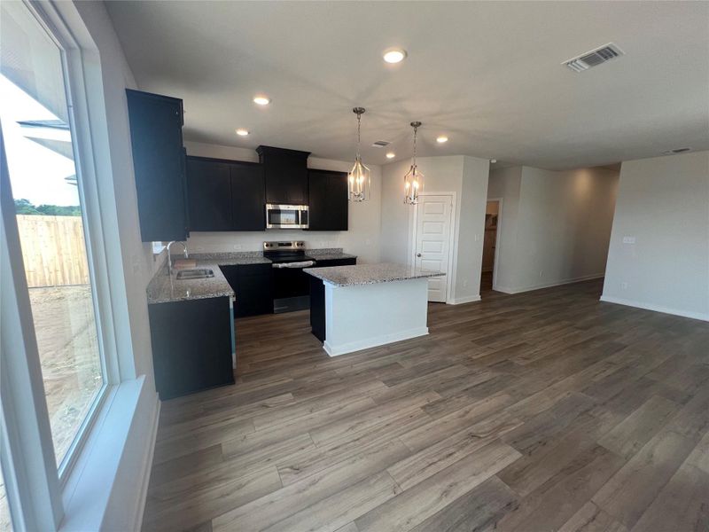 A contemporary kitchen features dark cabinetry, granite countertops, and modern pendant lighting over a central island.