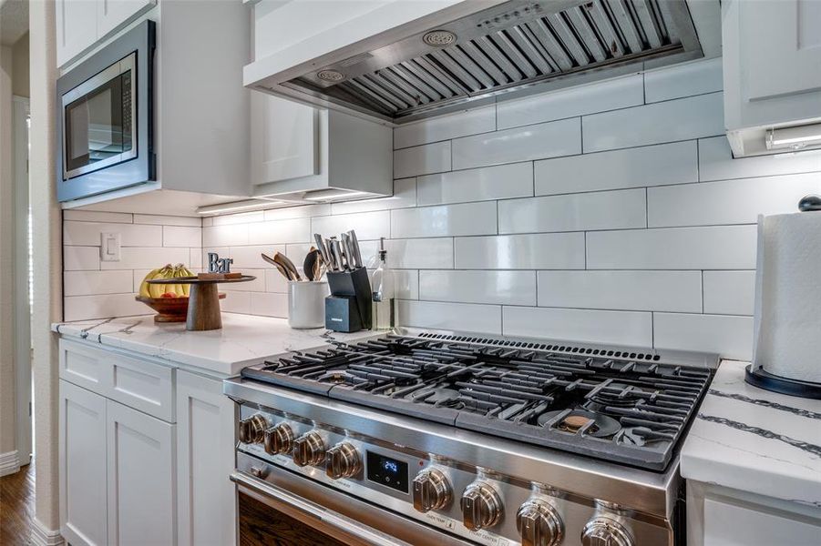 Kitchen featuring white cabinets, stainless steel appliances, extractor fan, and tasteful backsplash