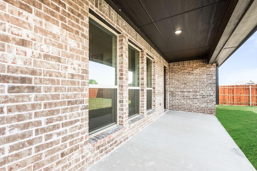 Covered back patio with brick exterior, dark ceiling, large windows, and fenced backyard with green lawn Covered back patio with brick exterior, dark ceiling, large windows, and fenced backyard with green lawn