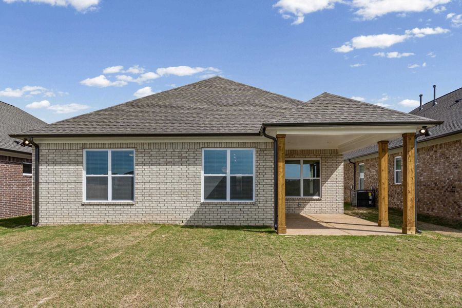 Back of property featuring a lawn, a shingled roof, a patio, and brick siding
