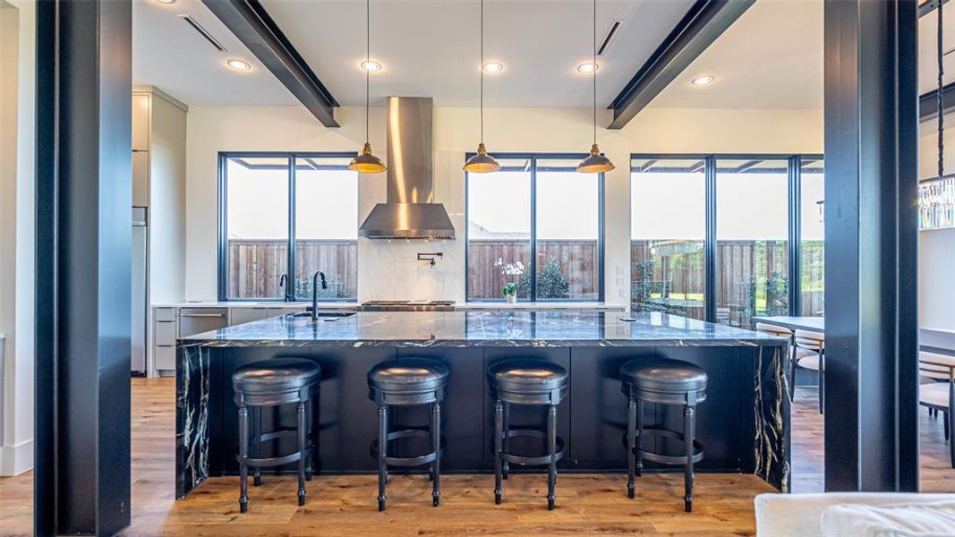 Kitchen with a kitchen bar, dark stone countertops, hanging light fixtures, and wall chimney range hood