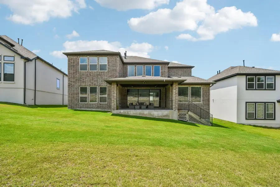 A vast, emerald lawn unfurls behind a two-story brick residence, boasting a generous covered patio perfect for outdoor living.