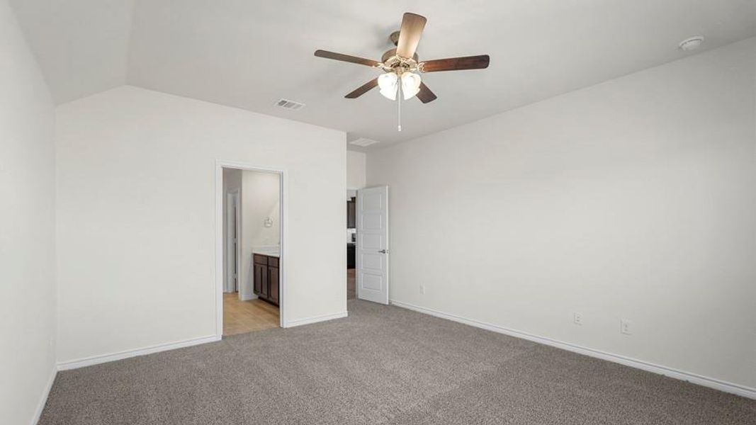 Spacious room with vaulted ceilings, carpeting, a ceiling fan, and access to an ensuite bathroom with a dark wood vanity