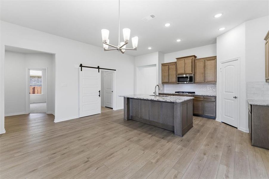 Kitchen featuring a barn door, hanging light fixtures, an island with sink, light stone counters, and a chandelier Kitchen featuring a barn door, hanging light fixtures, an island with sink, light stone counters, and a chandelier