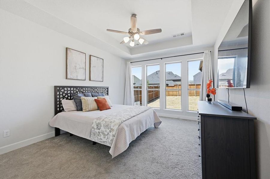 Primary bedroom featuring carpet floors, large windows providing natural light & a view into the backyard