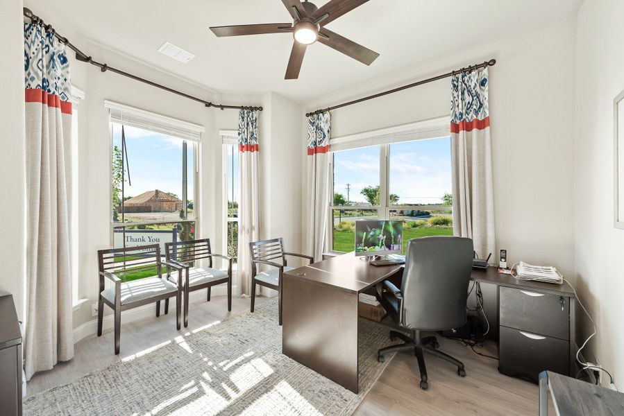Home office with dark wood desk, ceiling fan, and large windows with outdoor views Home office with dark wood desk, ceiling fan, and large windows with outdoor views