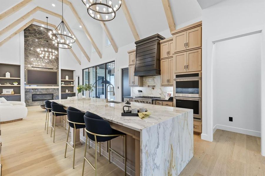 Kitchen with high vaulted ceiling, a glass covered fireplace, open floor plan, marble waterfall island with black quartz counters on either side Kitchen with high vaulted ceiling, a glass covered fireplace, open floor plan, marble waterfall island with black quartz counters on either side