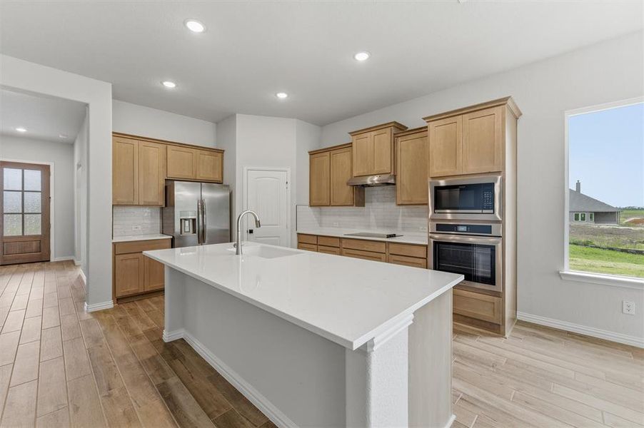 Kitchen featuring stainless steel appliances, an island with sink, decorative backsplash, light wood-style floors, and recessed lighting