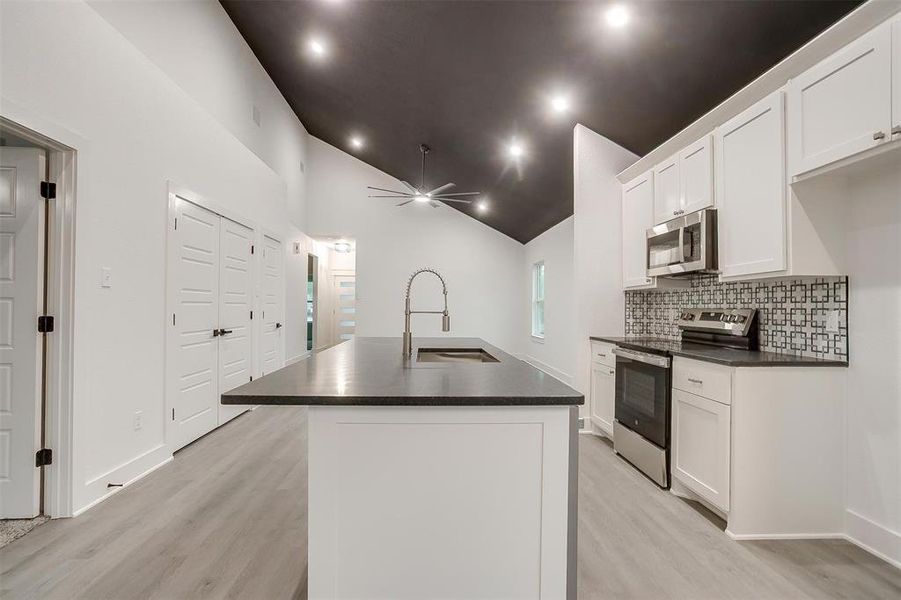 Kitchen with appliances with stainless steel finishes, dark countertops, light wood-style floors, and lofted ceiling