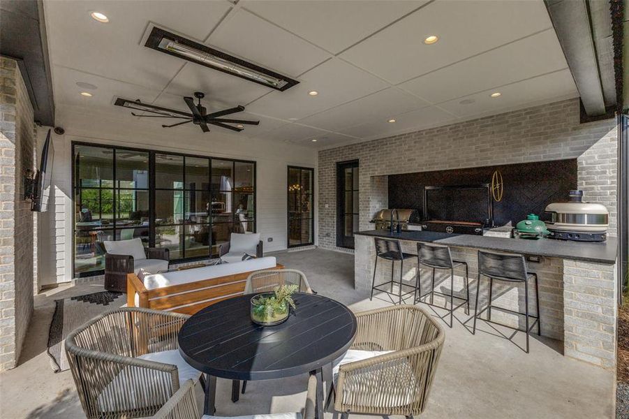 Outdoor covered patio featuring a full outdoor kitchen with bar seating, large multi-panel glass doors, a ceiling fan, recessed lighting, and a mounted heating element Outdoor covered patio featuring a full outdoor kitchen with bar seating, large multi-panel glass doors, a ceiling fan, recessed lighting, and a mounted heating element
