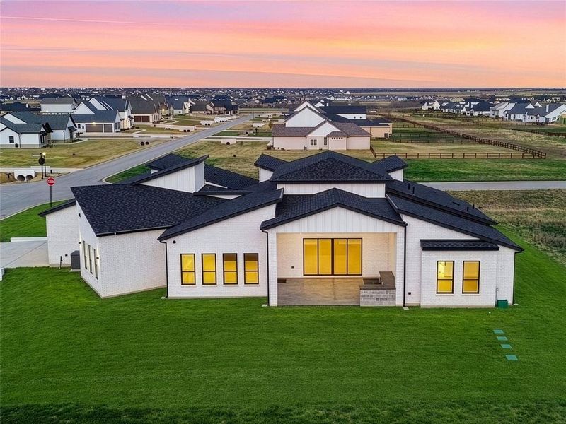 Twilight aerial showcasing the covered patio and spacious backyard with open views. Grass is digitally enhanced.