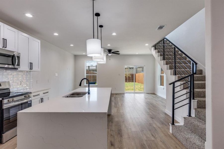 Kitchen with appliances with stainless steel finishes, decorative light fixtures, tasteful backsplash, white cabinets, and light wood finished floors Kitchen with appliances with stainless steel finishes, decorative light fixtures, tasteful backsplash, white cabinets, and light wood finished floors