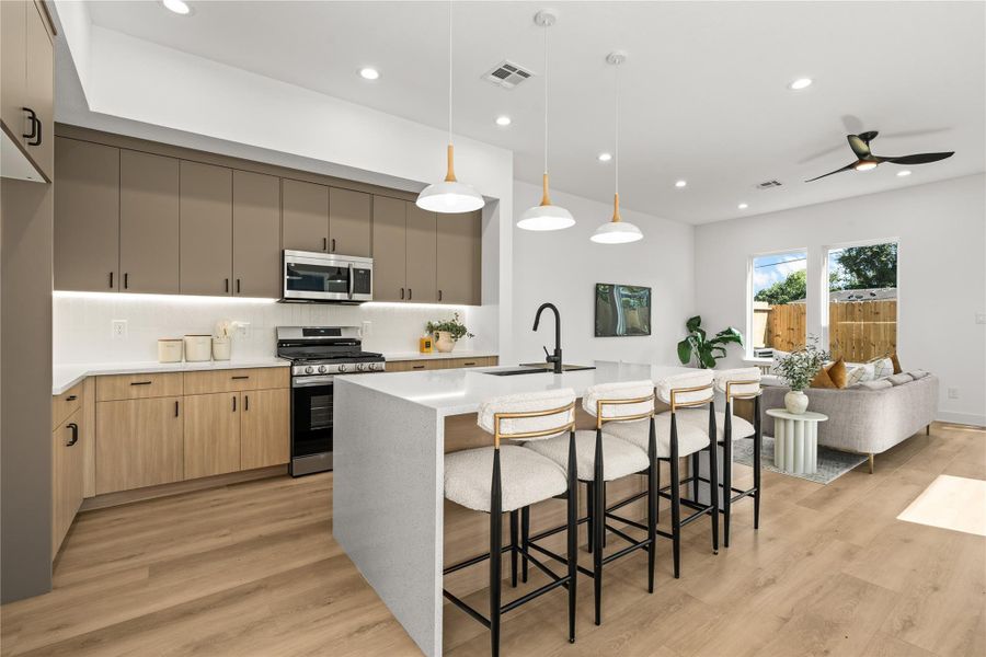 This setup includes a premium stainless steel appliance package with a gas range and built-in microwave, all set against a clean white vertical tile backsplash. The kitchen opens up directly to the living room, keeping the whole space connected while you cook.