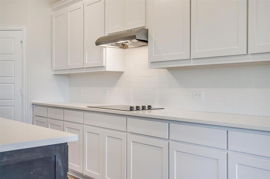 Kitchen with decorative backsplash, white cabinetry, black cooktop, and range hood