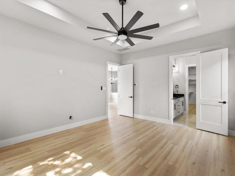 Spacious interior room featuring light wood-finish flooring, a contemporary ceiling fan, and a tray ceiling Spacious interior room featuring light wood-finish flooring, a contemporary ceiling fan, and a tray ceiling