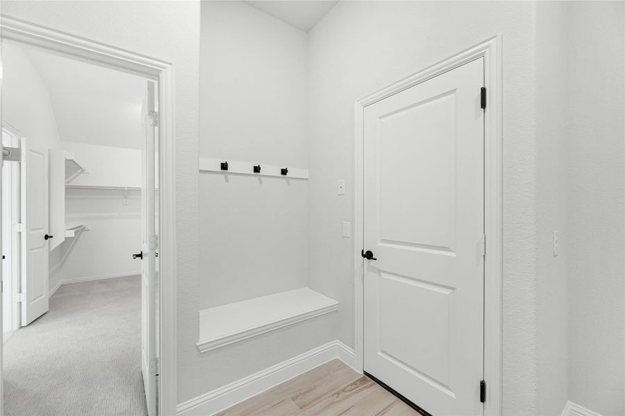 Mudroom entry with built-in bench, wall hooks, and white door leading to walk-in closet Mudroom entry with built-in bench, wall hooks, and white door leading to walk-in closet