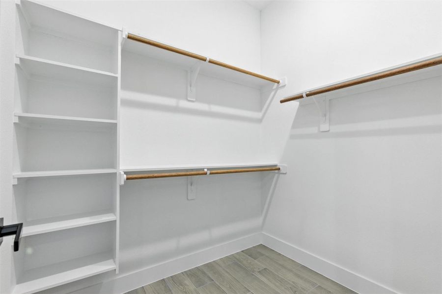 This is a spacious walk-in closet featuring multiple wooden hanging rods and built-in shelves, perfect for organized storage.