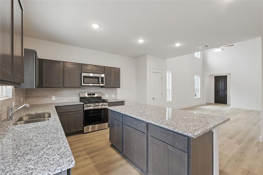 Kitchen with stainless steel appliances, dark wood finish cabinets, light stone countertops, light wood-style flooring, and a kitchen island