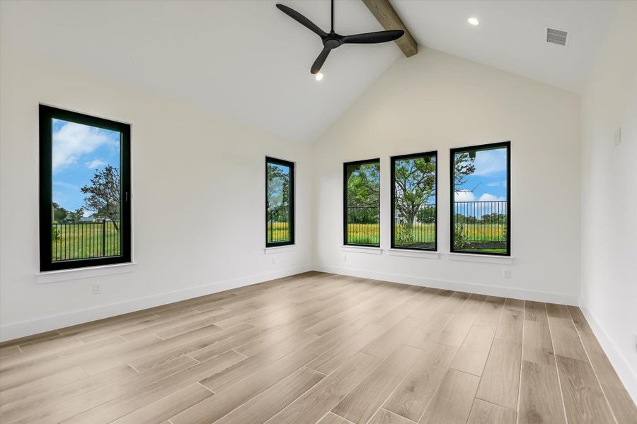 Spacious room featuring vaulted ceilings with an exposed beam, wood-finish flooring, and multiple windows with black trim