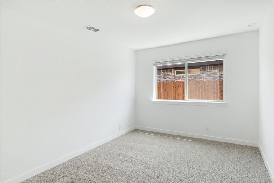 Empty bedroom with white walls, beige carpet, and a single window overlooking a wood fence