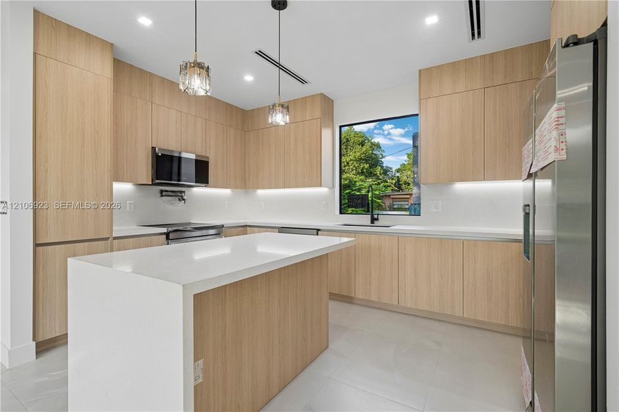 Kitchen featuring flat-panel wood-finish cabinetry, a waterfall-edge island, white countertops, recessed lighting, and stainless steel appliances Kitchen featuring flat-panel wood-finish cabinetry, a waterfall-edge island, white countertops, recessed lighting, and stainless steel appliances