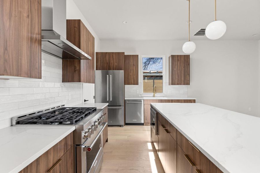 Kitchen with premium appliances, modern cabinets, wall chimney exhaust hood, and light wood finished floors