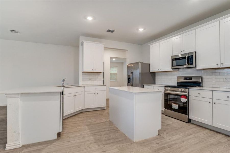 Kitchen featuring stainless steel appliances, white cabinetry, a peninsula, a kitchen island, and decorative backsplash