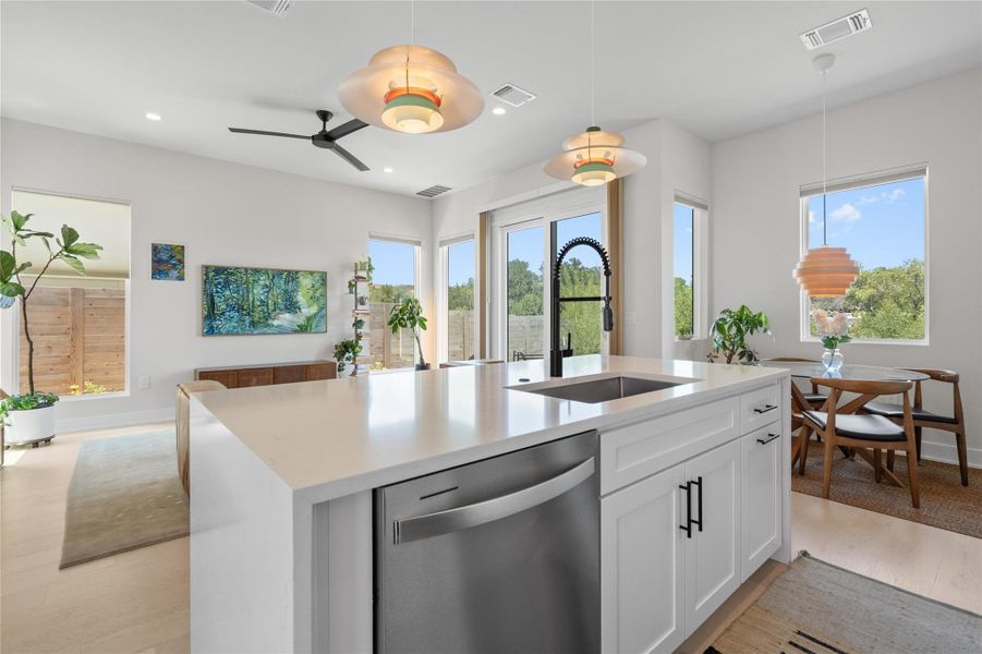 A well-lit kitchen with sleek white countertops and a modern sink overlooks a serene outdoor setting. A well-lit kitchen with sleek white countertops and a modern sink overlooks a serene outdoor setting.