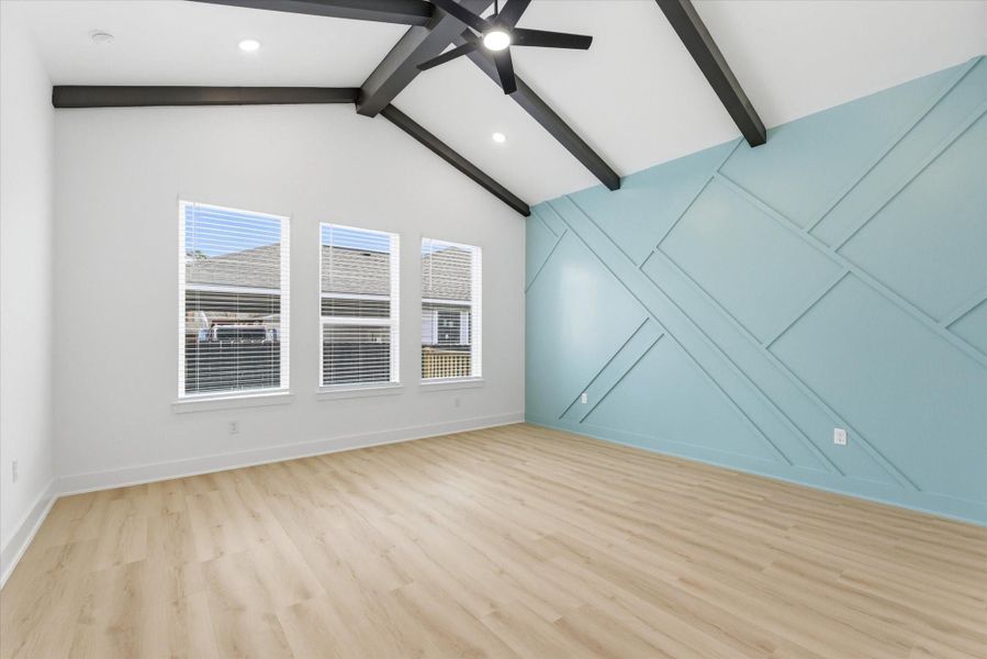 Amazing primary suite featuring soaring 12-foot vaulted ceilings with beams, a unique accent wall, and an abundance of natural and recessed lighting.