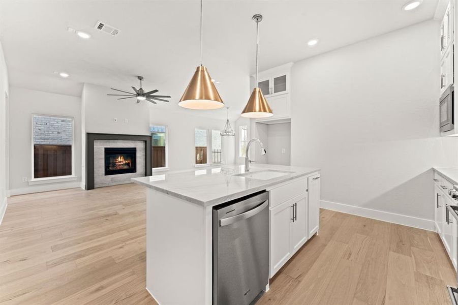 Kitchen with a tile fireplace, a center island with sink, white cabinets, stainless steel dishwasher, and light stone counters