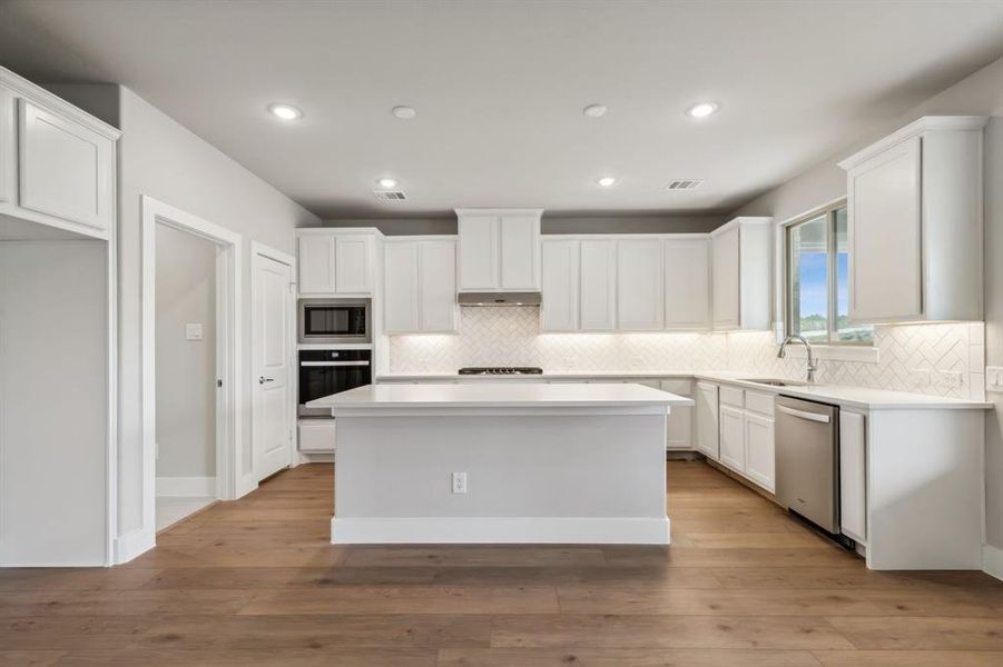 Kitchen with sink, light wood-type flooring, appliances with stainless steel finishes, a kitchen island, and white cabinetry