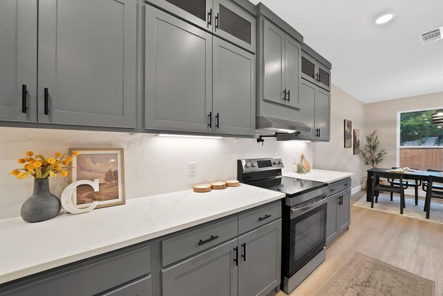 Modern kitchen featuring grey shaker-style cabinetry with matte black hardware, white countertops, and a stainless steel electric range Modern kitchen featuring grey shaker-style cabinetry with matte black hardware, white countertops, and a stainless steel electric range