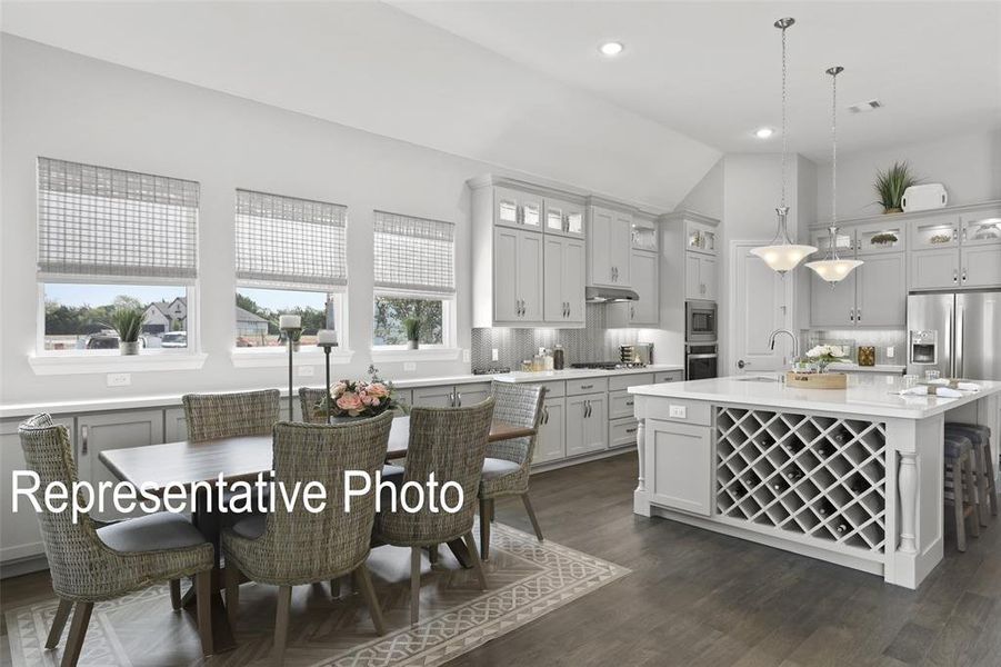 Open-concept kitchen featuring wood-finish flooring, light gray cabinetry, stainless steel appliances, a center island with built-in wine storage, and recessed lighting Open-concept kitchen featuring wood-finish flooring, light gray cabinetry, stainless steel appliances, a center island with built-in wine storage, and recessed lighting