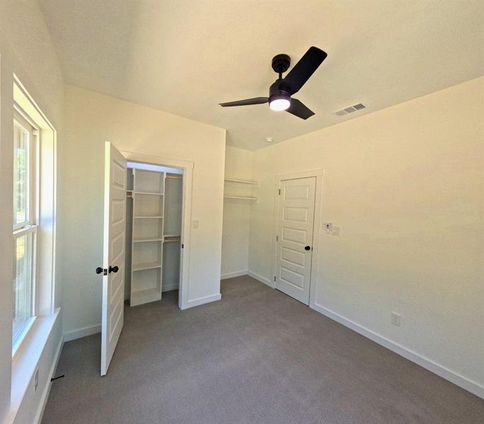 Unfurnished bedroom with carpet floors, ceiling fan, and a walk in closet Unfurnished bedroom with carpet floors, ceiling fan, and a walk in closet